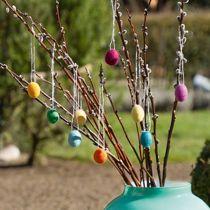 Bunte Filzeier h&auml;ngen an braunen Zweigen in einer t&uuml;rkisfarbenen Vase, weicher Filz, frische Fr&uuml;hlingsfarben.