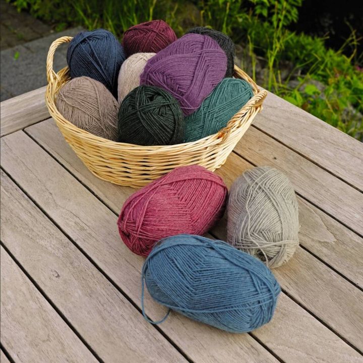 Mehrere Wollknäuel in verschiedenen Farben, darunter Blau, Rot und Grau, in einem Korb und auf einem Holztisch. Geeignet für Strick- oder Häkelprojekte.