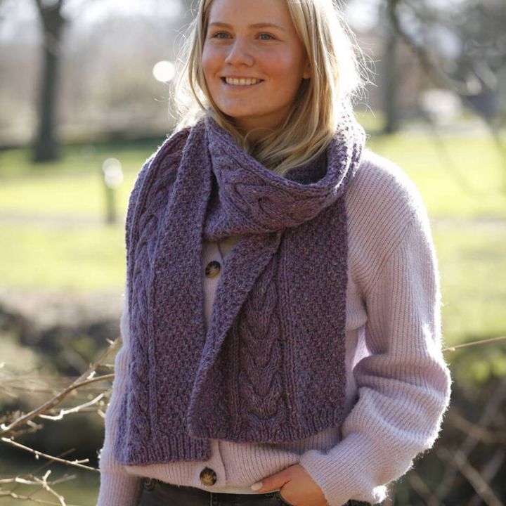 Junge Frau mit langem, lila Wollschal und passendem Pullover, grobe Strickstruktur, drau&szlig;en im hellen Tageslicht.