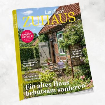 Titelbild der Zeitschrift „Landlust Zuhause“ zeigt eine idyllische Gartenszene mit einem Backsteinhaus und bunter Bepflanzung. Schlagzeilen thematisieren Sanierung eines alten Hauses, Gartenmöbel, Innenhofgestaltung und Handarbeiten im Sommer.