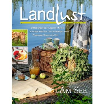 Titelbild der Zeitschrift „Landlust“ Juli/August 2022. Ein Picknickkorb, grüne Tassen, ein Kranz aus Zweigen und eine Decke auf einem Steg am See. Inset-Bilder zeigen Kühe und ein Dessert. Themen: Entdeckungsreise, Sonnensegel, Pflegewege.