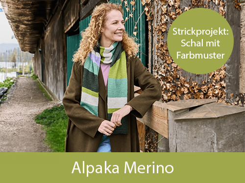 Eine lächelnde Frau trägt einen selbstgestrickten, gestreiften Schal aus Landlust Alpaka-Merino 160. Im Hintergrund ist ein Stallgebäude zu sehen. Oben rechts steht „Strickprojekt: Schal mit Farbmuster". Bild verlinkt zur Alpaka-Merino.