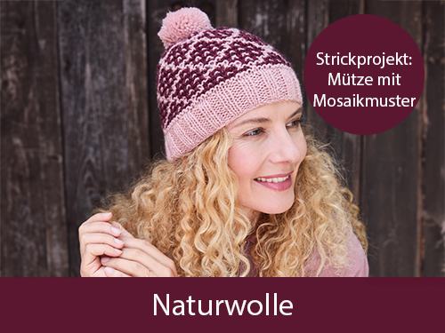 Eine lächelnde Frau trägt eine selbst gestrickte rosa-burgundfarbende Mütze. Sie ist vor einer Holzwand. Text: Strickprojekt Mütze mit Mosaikmuster. Das Bild verlinkt auf die passende Wolle: Naturwolle im Landlust Shop
