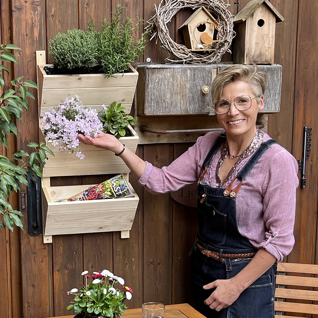 Wandbeet mit drei hellen Holzk&auml;sten, bepflanzt mit gr&uuml;nen Kr&auml;utern vor einer dunkelgrauen Holzwand.