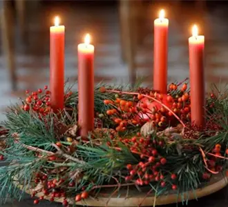 Ein Adventskranz auf Tannenzweigen und roten Beeren auf dem vier rote Kerzen brennen.