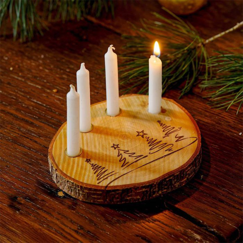 Eine Baumscheibe mit reingelaserten Tannenbäumen liegt auf einem Holztisch. In der Baumscheibe stecken vier weiße Kerzen