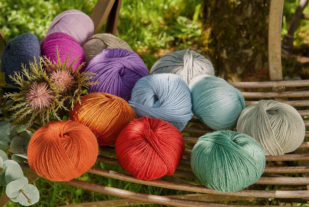 Wolle in unterschiedlichen Farben liegt auf einem Holzkonstrukt in der Natur