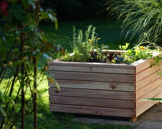 Holzhochbeet im Garten mit verschiedenen Kräutern und Salatpflanzen, umgeben von Gras und Sträuchern. Bild verlinkt zum Workshop.
