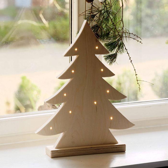 Ein Tannenbaum aus Holz stecht auf einer Fensterbank. Einzelne kleine Lichter sind darauf verteilt.