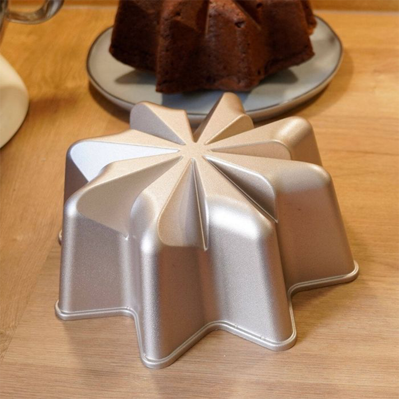 Eine Metall-Backform in Form eines Sterns liegt auf einer Holzoberfläche. Im Hintergrund befindet sich ein gebackener Kuchen