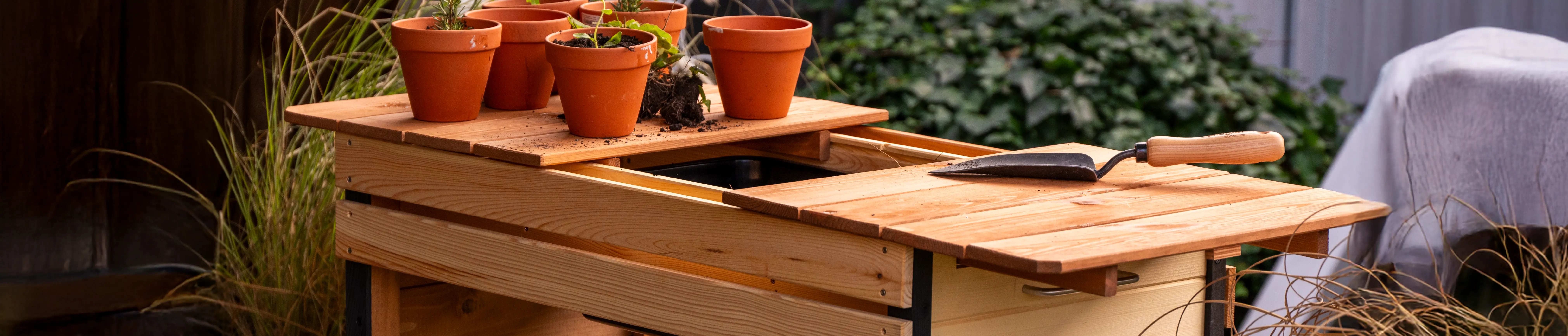 Gartenarbeitstisch steht im Freien. Auf ihm stehen Blument&ouml;pfe und liegt eine Pflanzenkelle