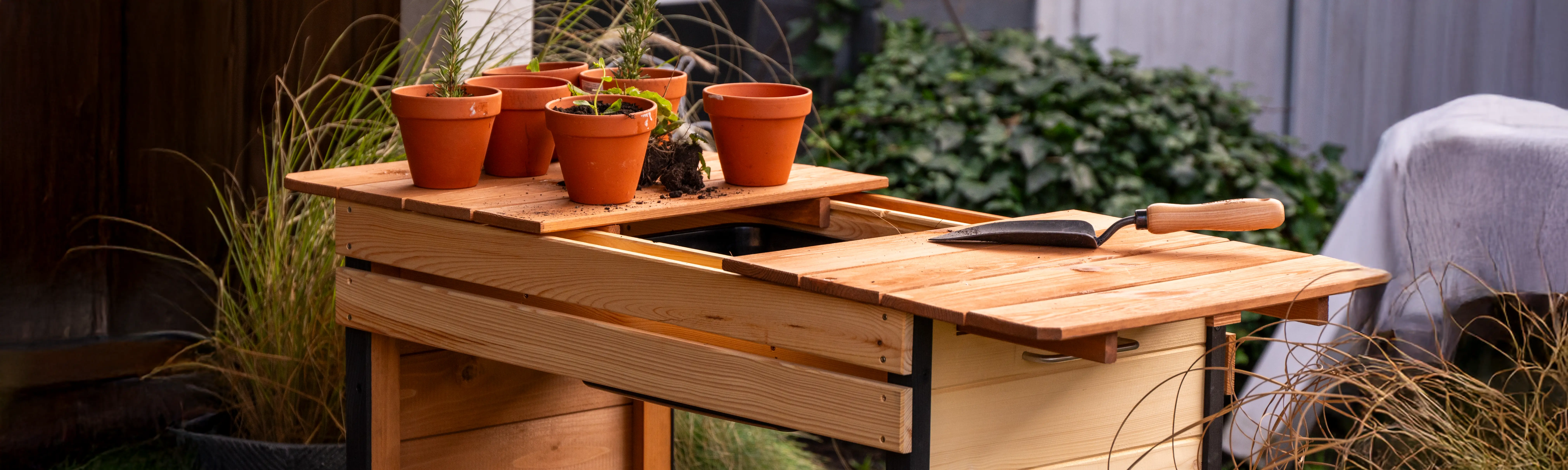 Gartenarbeitstisch steht im Freien. Auf ihm stehen Blument&ouml;pfe und liegt eine Pflanzenkelle