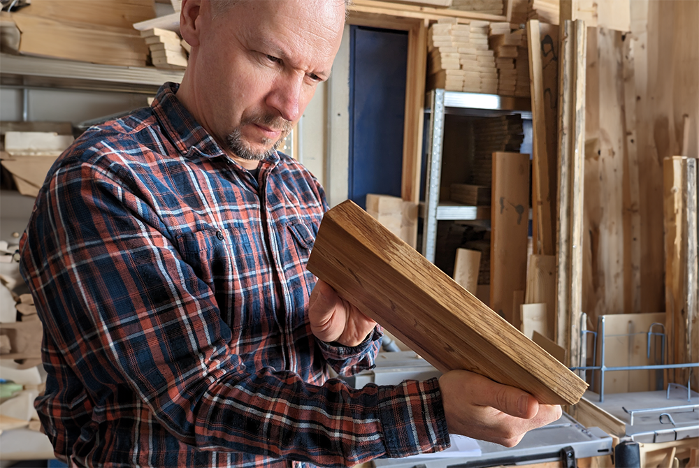 Ein Mann hält ein Stück Holz in der Hand und prüft etwas sehr konzentriert nach