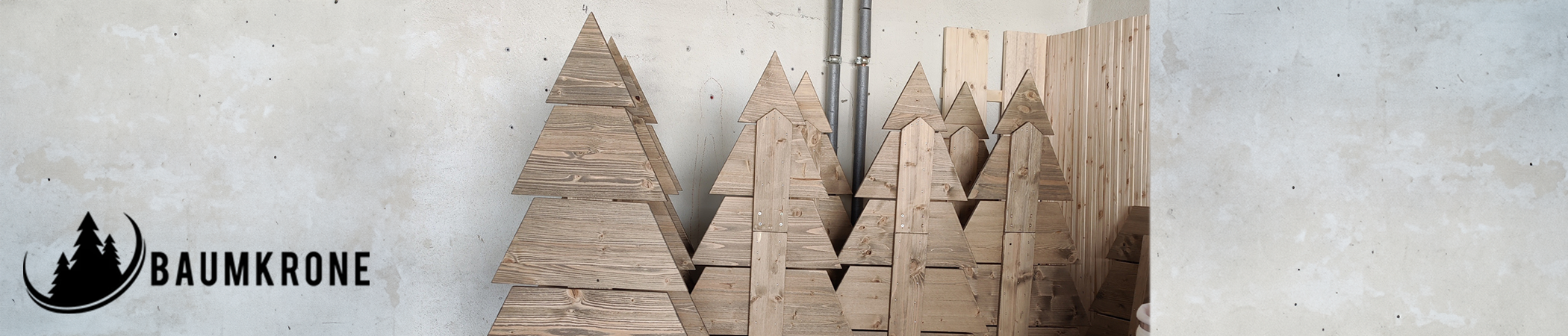 Vor einer grauen Betonwand stehen Bäume aus Holz