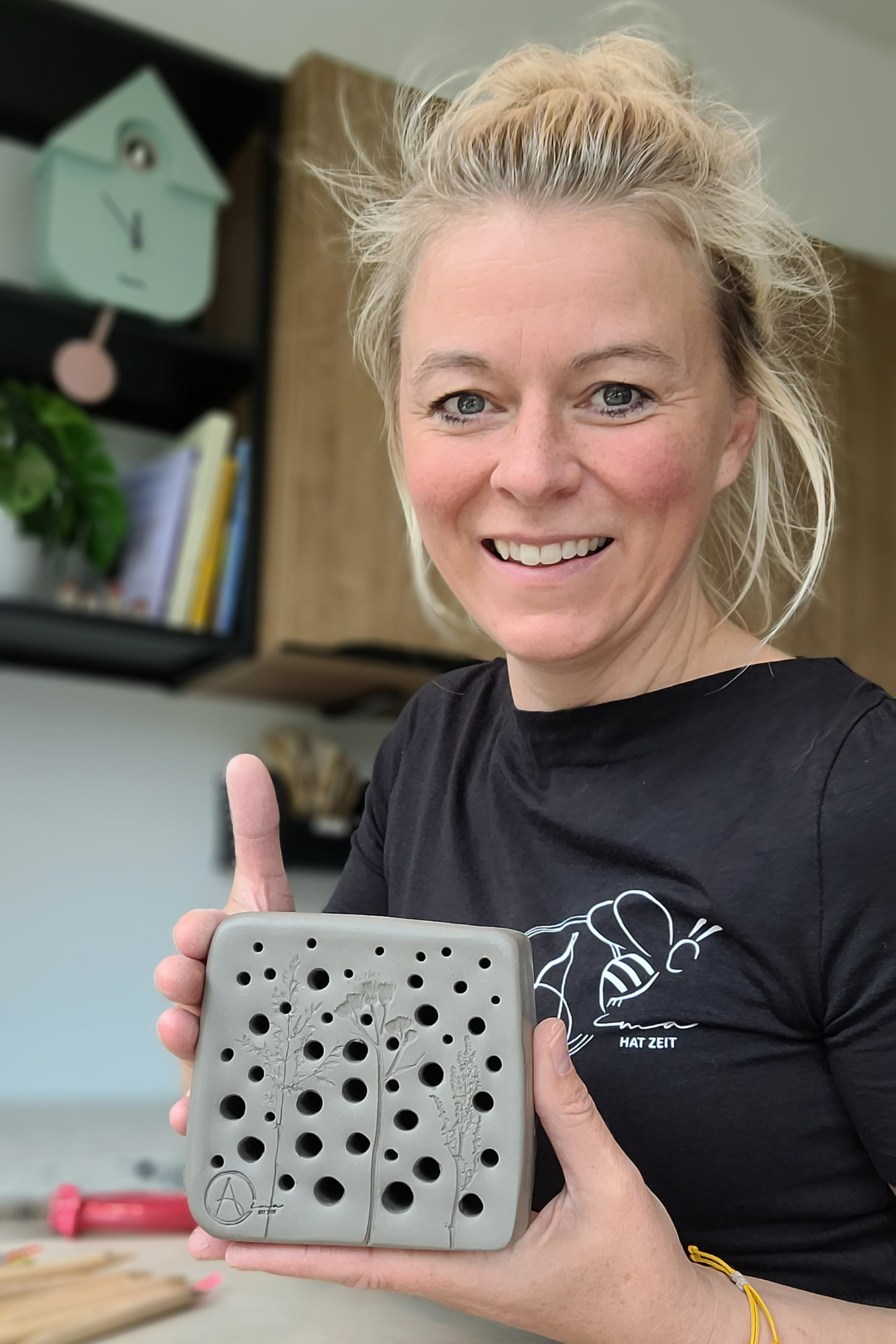 Frau h&auml;lt grau-quadratischen Tonblock mit vielen runden L&ouml;chern, glatte und matte Oberfl&auml;che, dezente Umgebung im Hintergrund.