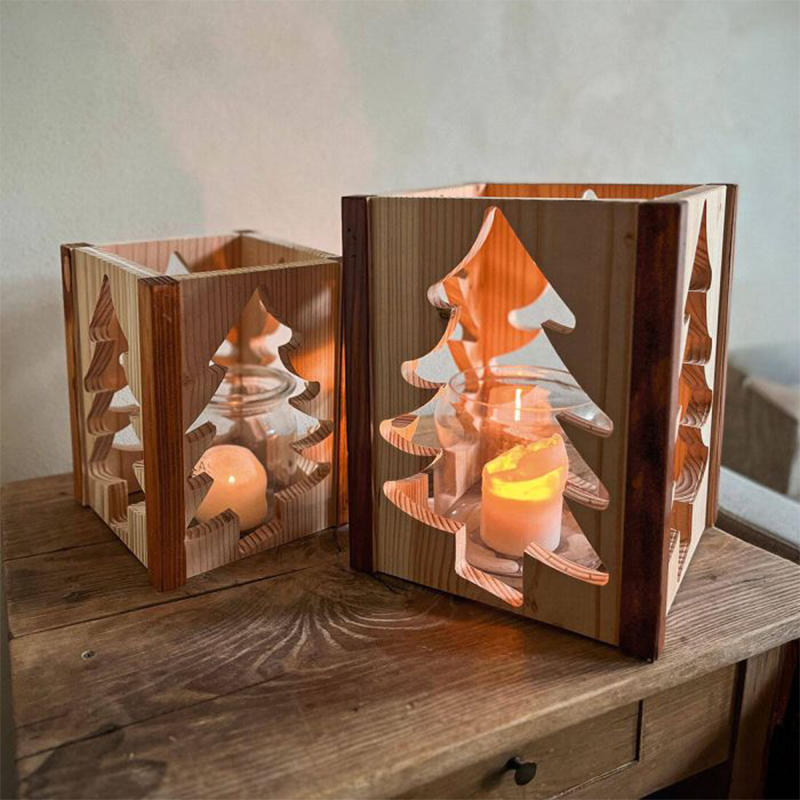 Ein Windlicht aus Holz mit ausgeschnittenen Tannen-Form steht auf einem Holztisch