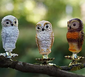 Drei Tannenbaumschmuck-Figuren in Form von Eulen sind auf einem Zweig befestigt. Die Eulen sind in weiß und braun Tönen gefärbt.