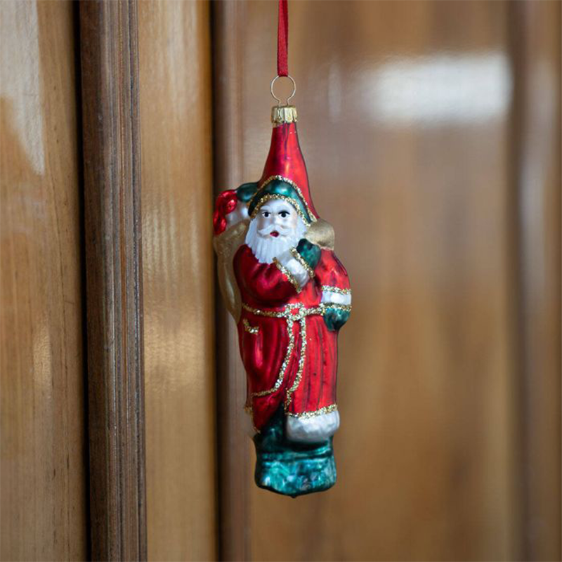 Eine Glasfigur mit Aussehen eines Weihnachtsmann hängt neben einer Wand aus Holz