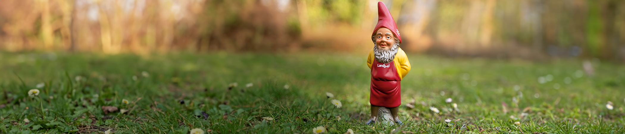 Ein rot-gelber Gartenzwerg mit Landlust-Schürze steht auf einer grünen Wiese