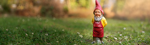 Ein rot-gelber Gartenzwerg mit Landlust-Schürze steht auf einer grünen Wiese