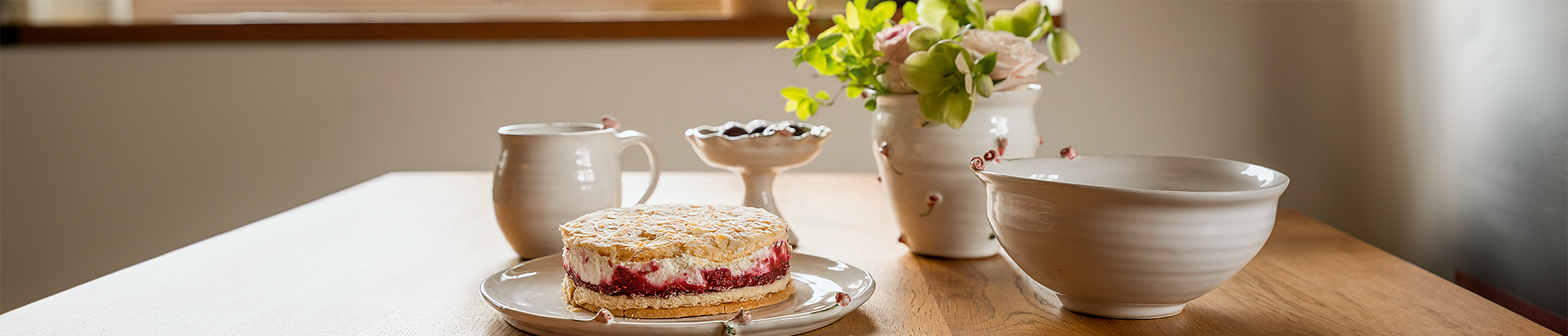 Auf einem Holztisch steht unterschiedliche weiße Keramik mit kleinen Rosen-Details
