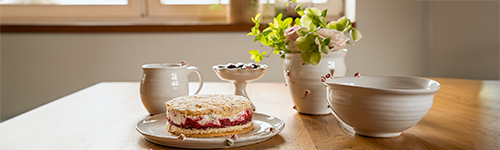 Auf einem Holztisch steht unterschiedliche weiße Keramik mit kleinen Rosen-Details