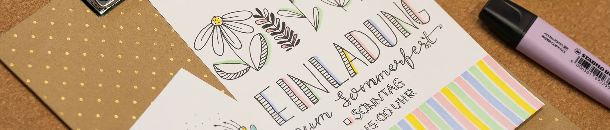 Einladungsdesign auf einem Tisch liegend, mit handgezeichneten Blumen und dem Text "Einladung zum Sommerfest". Darunter Details: Datum, Uhrzeit. Daneben liegt ein lila Textmarker. Hintergrund: Braunes Papier mit goldenen Punkten.