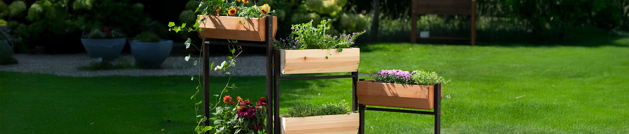 Vertikalbeet mit 5 K&auml;sten aus hellem Holz, schwarze Metallstreben, bunte Pflanzen und gr&uuml;ner Rasen im Hintergrund.