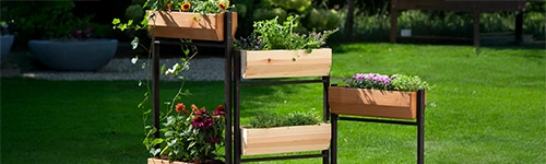 Vertikalbeet mit 5 K&auml;sten aus hellem Holz, schwarze Metallstreben, bunte Pflanzen und gr&uuml;ner Rasen im Hintergrund.