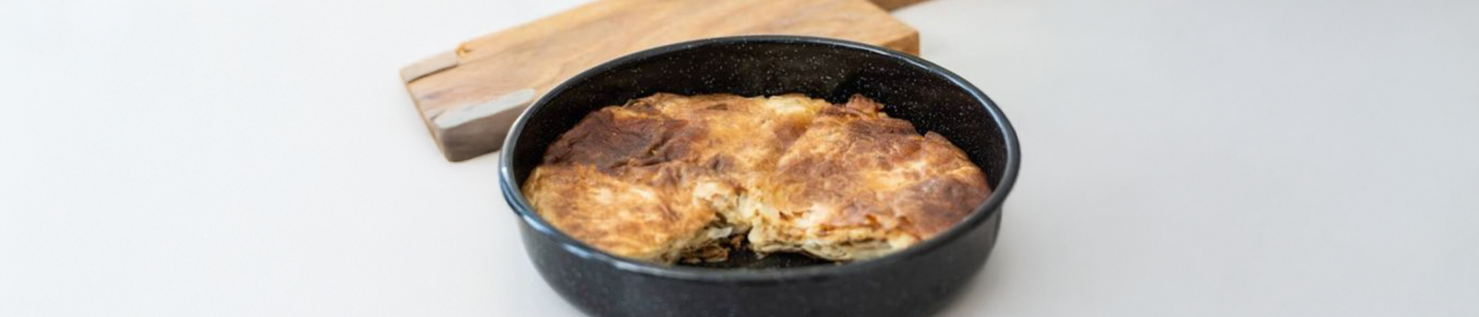 Eine Form aus Emaille in der Kartoffelgratin zubereitet wurde. Im Hintergrund liegt ein Holzbrett