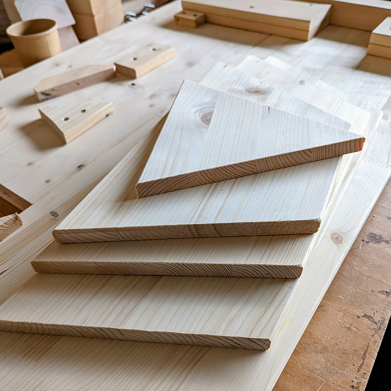 Mehrere zugeschnittene Holzstücke liegen aufeinander auf dem Boden