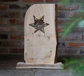 Eine Holzscheibe in die ein Loch in Form von einem Stern reingeschnitten wurde. Der Stern wird von einer Lichterkette beleuchtet.
