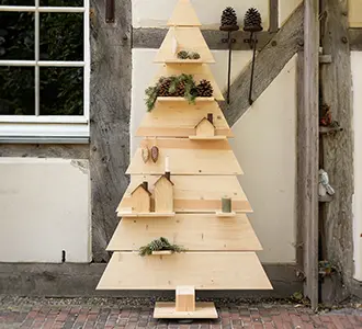 Vor einem Fachwerkhaus steht ein gezimmerter Weihnachtsbaum. Er ist mit Tannenzweigen und Tannenzapfen dekoriert.