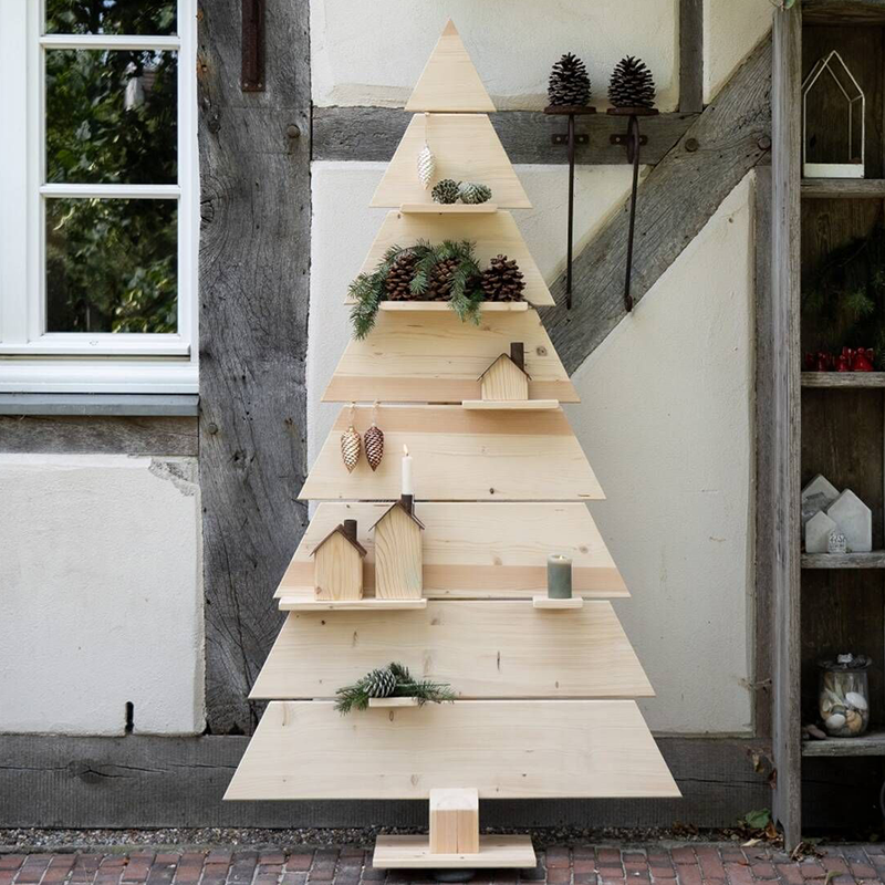 Vor einem Fachwerkhaus steht ein gezimmerter Weihnachtsbaum. Er ist mit Tannenzweigen und Tannenzapfen dekoriert.