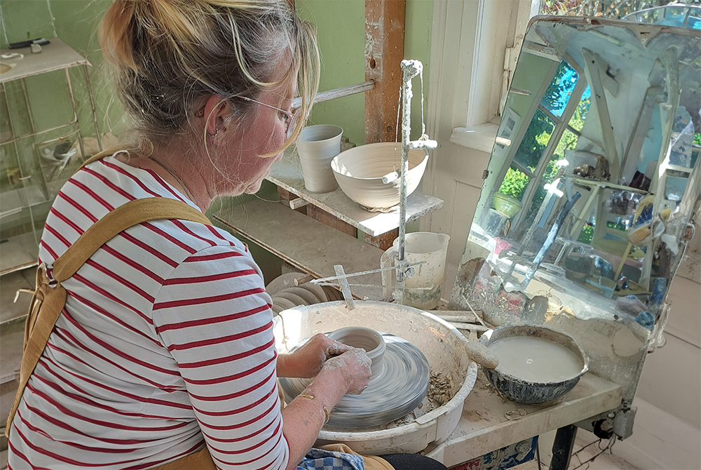 Eine Person im gestriften Oberteil sitzt an einer Drehscheibe und stellt Keramik her