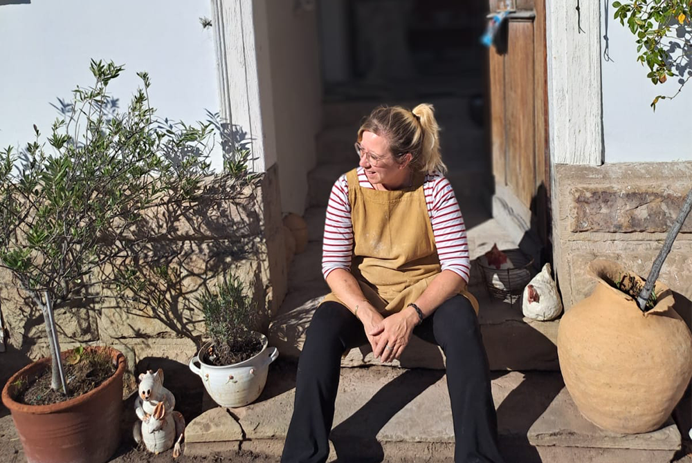 Eine Frau mit brauner Schürze sitzt auf den Stufen vor einem Haus