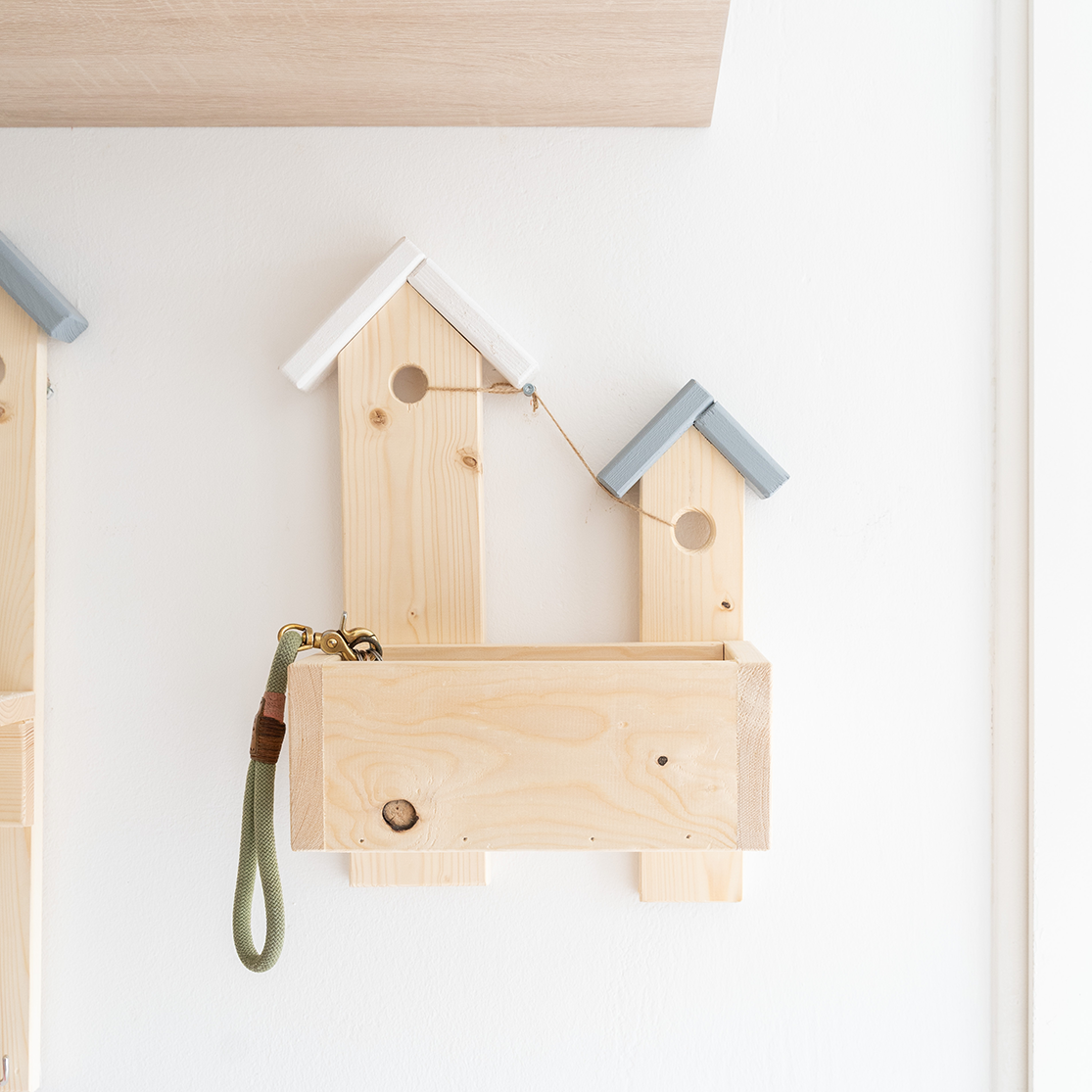 Helles Holzregal in Vogelhausform mit wei&szlig;en und grauen D&auml;chern, glatte Oberfl&auml;che, goldene Geldb&ouml;rse und Brille im Fach.