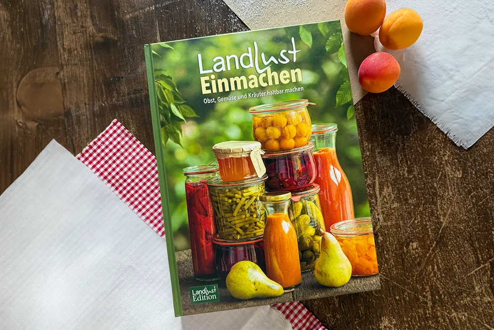 Das Landlust-Buch "Einmachen" liegt auf einem Holztisch, umgeben von Tischtüchern und Nektarinen