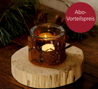 Ein Kerzenhalter ist von einem Häuserkranz aus Rostpanina umgeben und steht auf einer Holzscheibe.