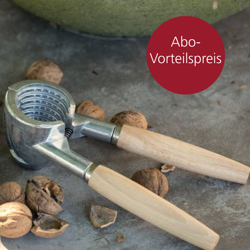 Ein Nussknacker mit Holzgriff liegt auf einer Steinplatte. Daneben sind Haselnüsse verteilt.