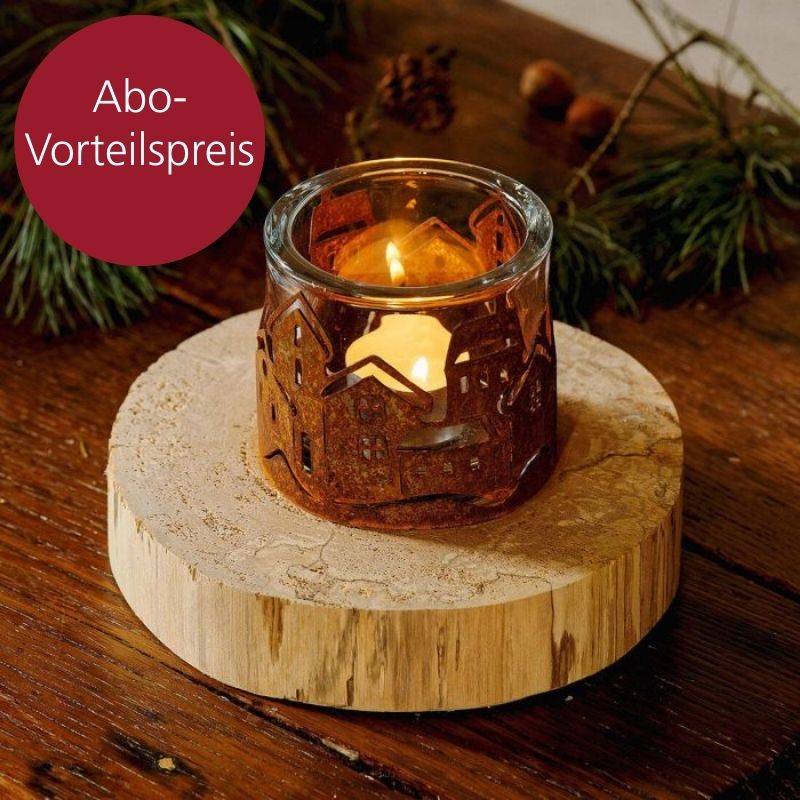 Ein Kerzenhalter ist von einem Häuserkranz aus Rostpanina umgeben und steht auf einer Holzscheibe.