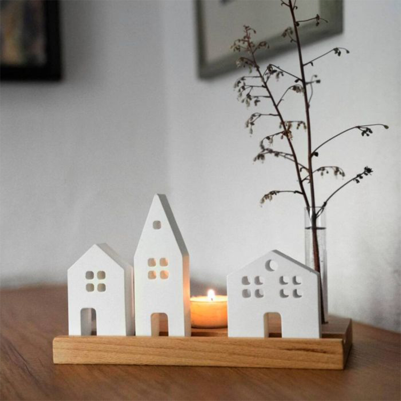 Kleine weiße Häuschen stehen auf einem Holzbrett. Darauf ist auch eine kleine Vase und ein Teelicht dekoriert
