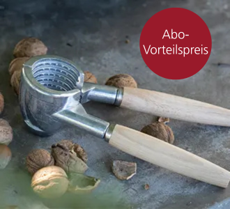 Ein Nussknacker mit Holzgriff liegt auf einer Steinplatte. Daneben sind Haselnüsse verteilt.