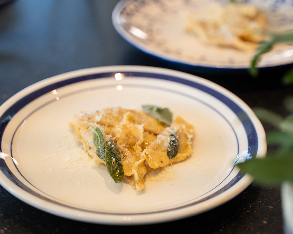 Auf einem weißen Teller mit blauem Rand ist Pasta mit Parmesan und Salbeiblättern angerichtet