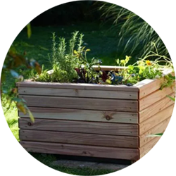 Ein quadratischer Pflanzkasten aus Holz steht bepflanzt im freien.