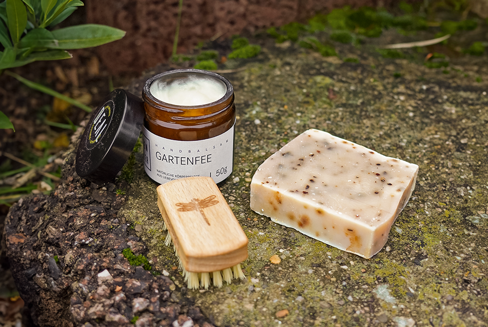 Eine Bürste, Seife und eine Creme stehen draußen auf einem Stein