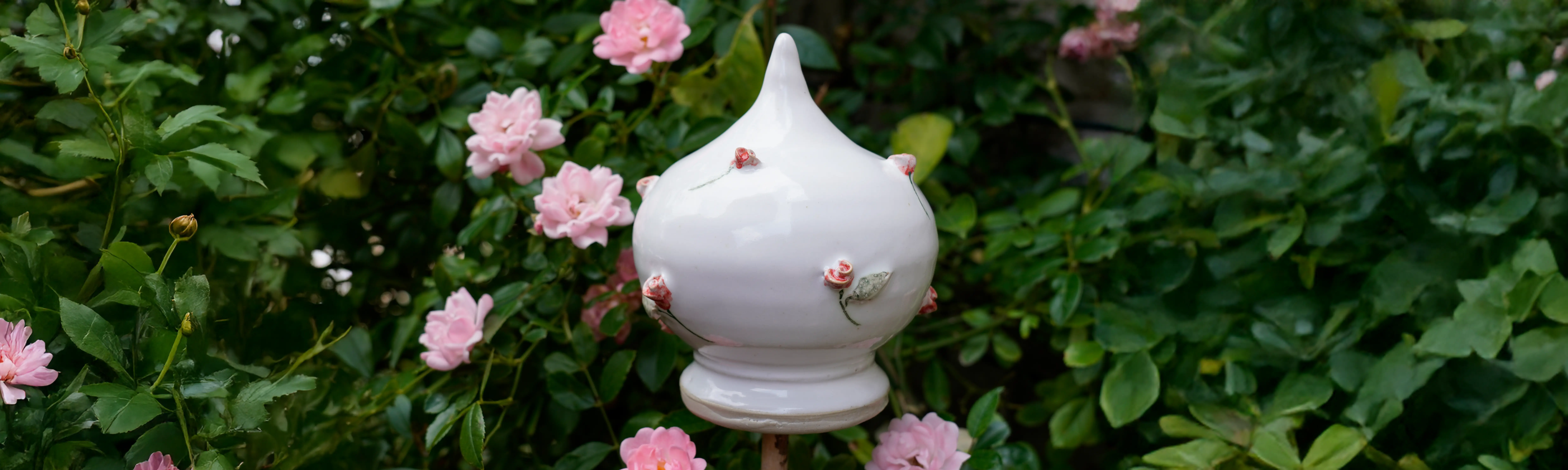 Eine Rosenkugel aus Keramik steht auf einem Stab in einem Blumenbusch.