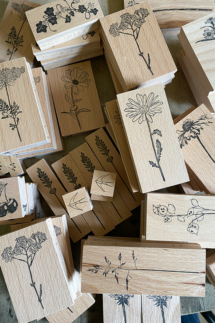 Frau mit blondem Haar formt Ton an einem Tisch, gr&uuml;ne Pflanze im Hintergrund, warme Farben, kreative Atelier-Atmosph&auml;re.