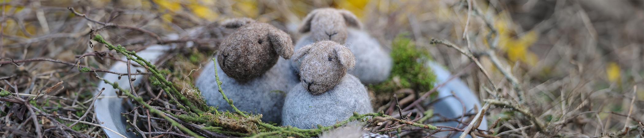 Drei Schafe aus Filz sitzen in einem Nest aus Zweigen und Moos