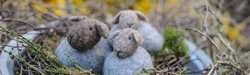 Drei Schafe aus Filz sitzen in einem Nest aus Zweigen und Moos